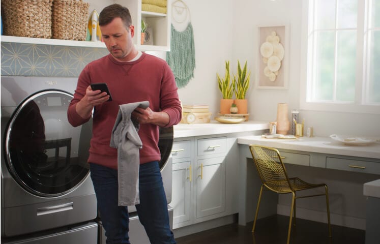A person holding a smartphone in the laundry room with the home heartbeat blog logo