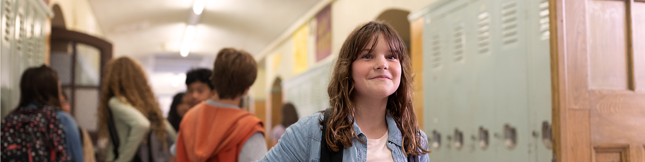 A smiling child in a school hallway with other kids behind them
