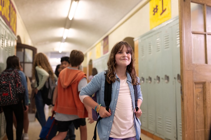A smiling child in a school hallway with other kids behind them