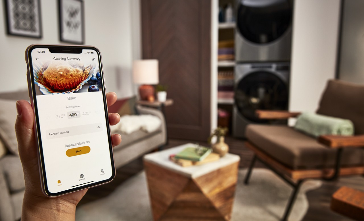 Closeup of a person holding a smartphone with the Whirlpool® App on the screen and a living area in the background