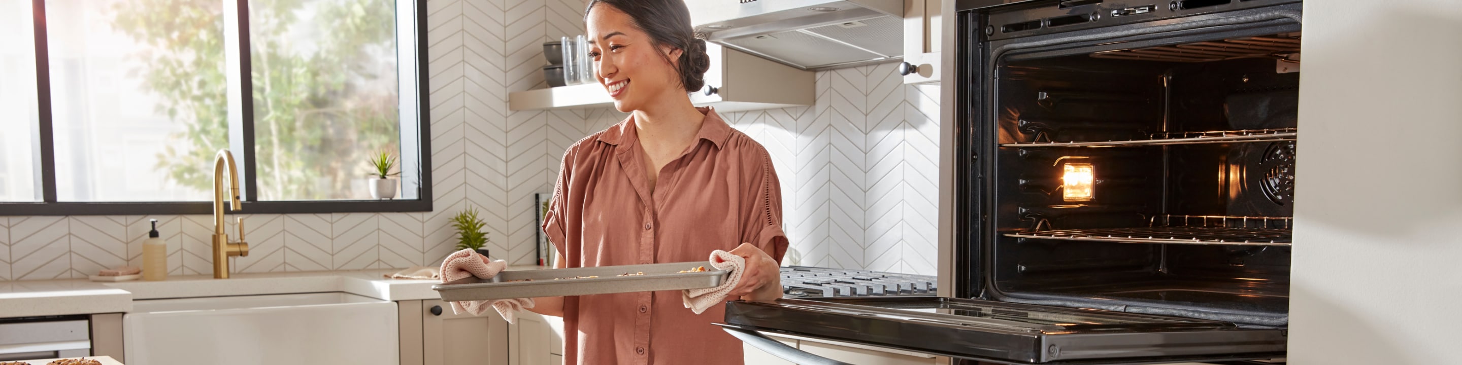A person removing a tray of food from a Whirlpool® Wall Oven