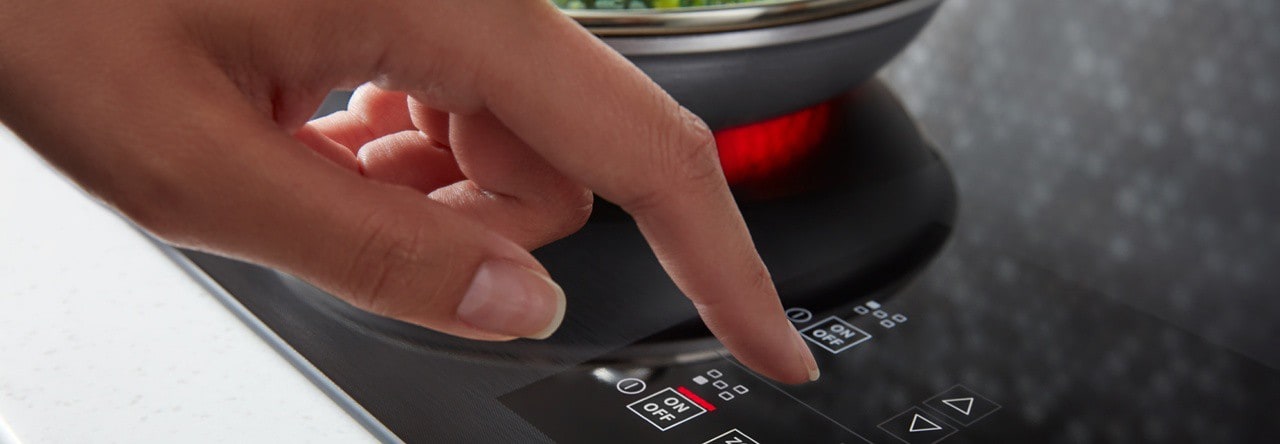 A hand selecting a cooking setting on a stovetop with the latest cooking technology. A hand selecting a cooking setting on a stovetop with the latest cooking technology.