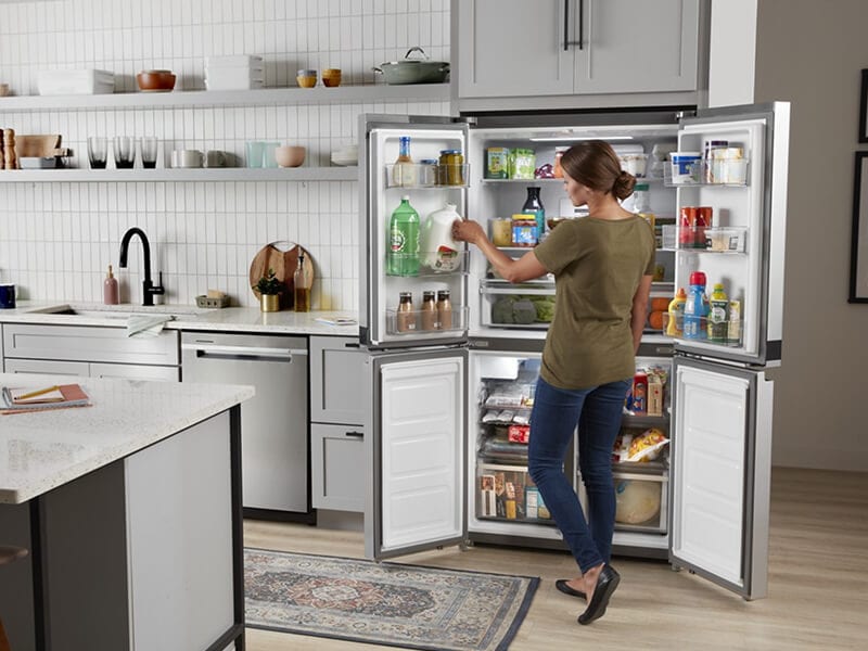 Person stocking the in-door shelving of an open Whirlpool® 4-Door Refrigerator Person stocking the in-door shelving of an open Whirlpool® 4-Door Refrigerator