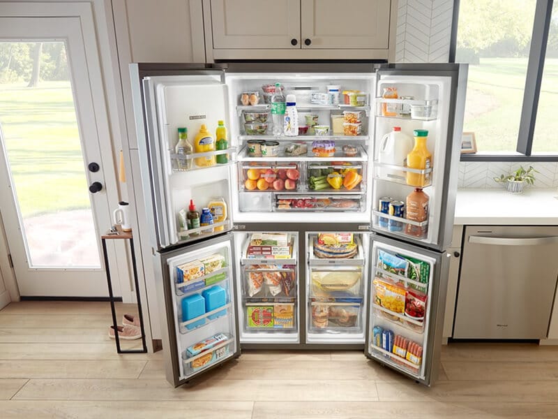 Fully stocked, open 4-door refrigerator built into tan cabinetry Fully stocked, open 4-door refrigerator built into tan cabinetry