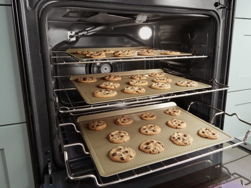 Three trays of cookies baking in an oven Three trays of cookies baking in an oven
