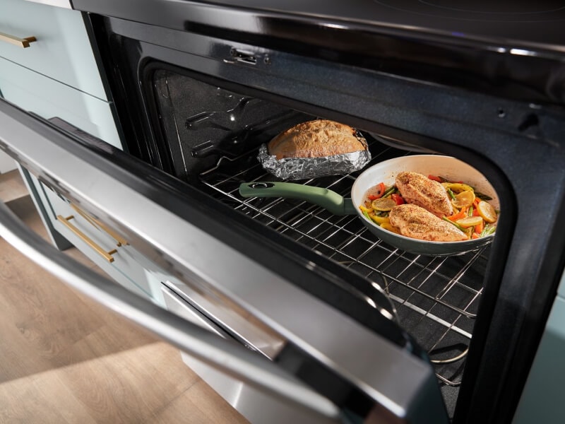 A chicken meal cooking in the oven with a loaf of bread A chicken meal cooking in the oven with a loaf of bread