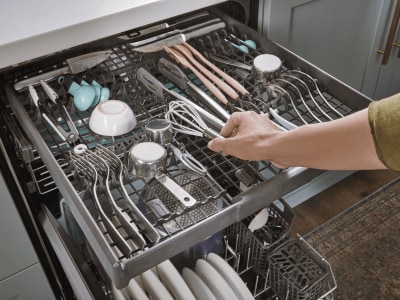 Person placing items on the 3rd rack of a dishwasher