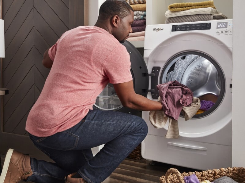 Person loading laundry into a white Whirlpool® Front Load Washer Person loading laundry into a white Whirlpool® Front Load Washer