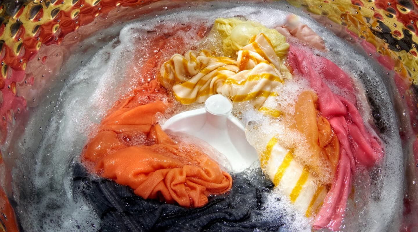 Colorful laundry load soaking inside of a top load washer with an agitator Colorful laundry load soaking inside of a top load washer with an agitator
