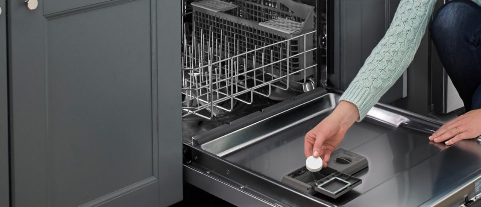 A person adding a dishwasher cleaner tablet to a dishwasher A person adding a dishwasher cleaner tablet to a dishwasher