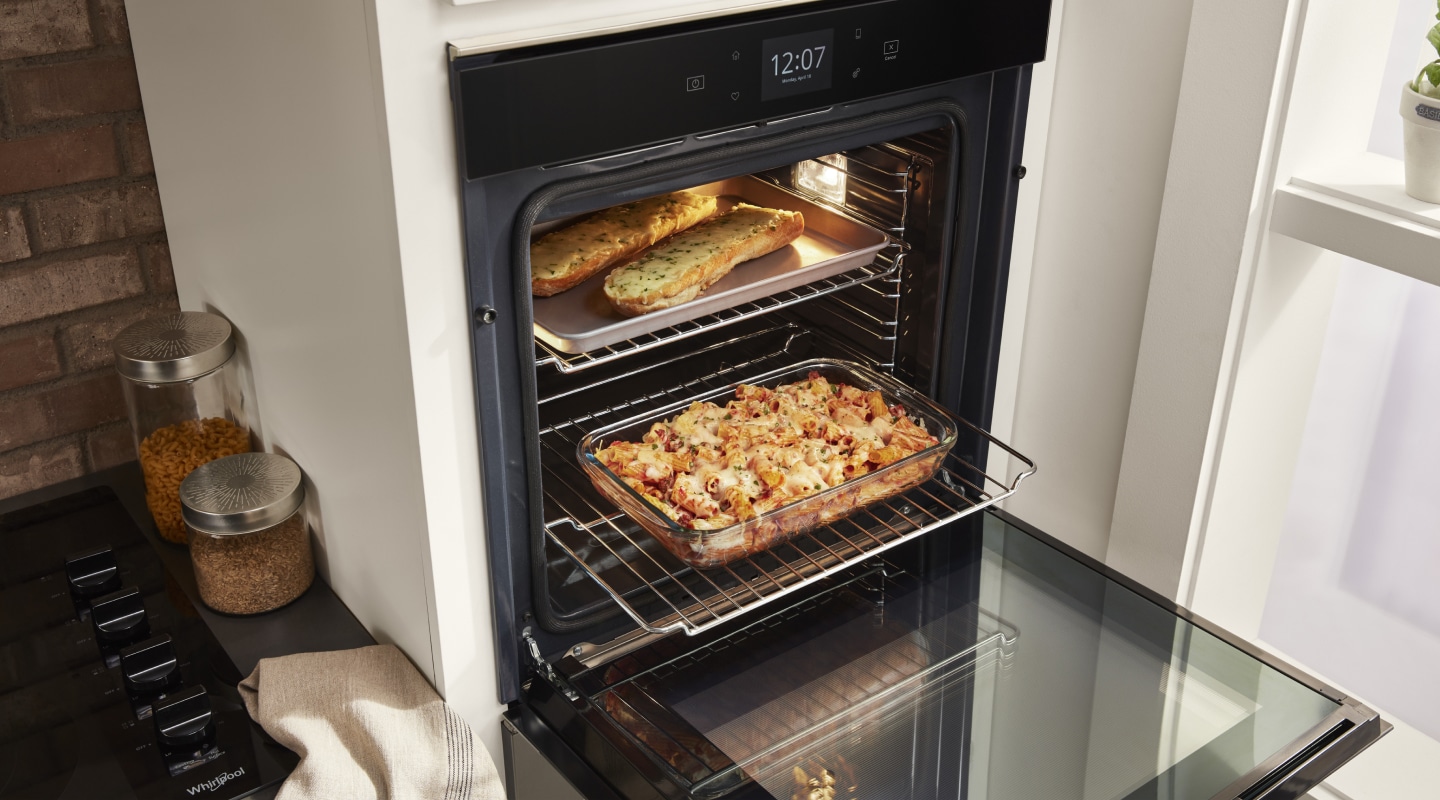 Open Whirlpool®  single wall oven showing a tray of garlic bread and casserole dish Open Whirlpool®  single wall oven showing a tray of garlic bread and casserole dish