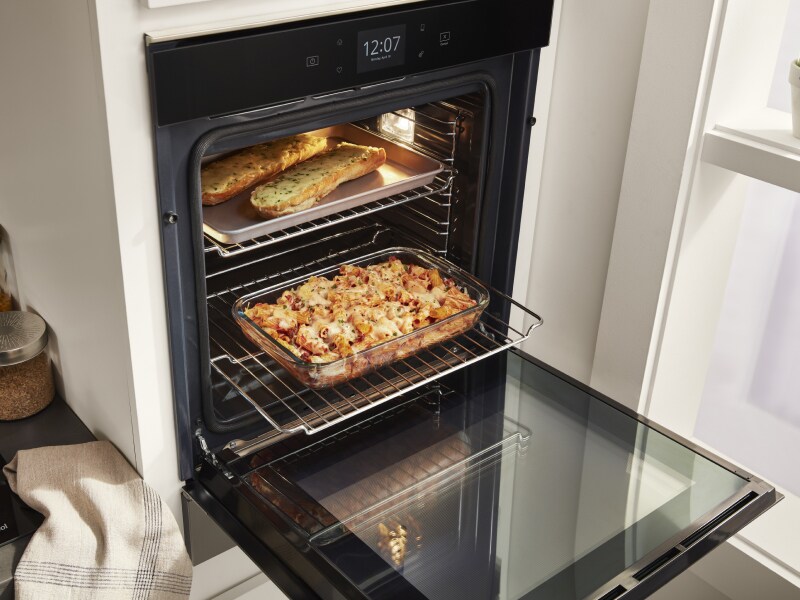 Open Whirlpool®  single wall oven showing a tray of garlic bread and casserole dish Open Whirlpool®  single wall oven showing a tray of garlic bread and casserole dish
