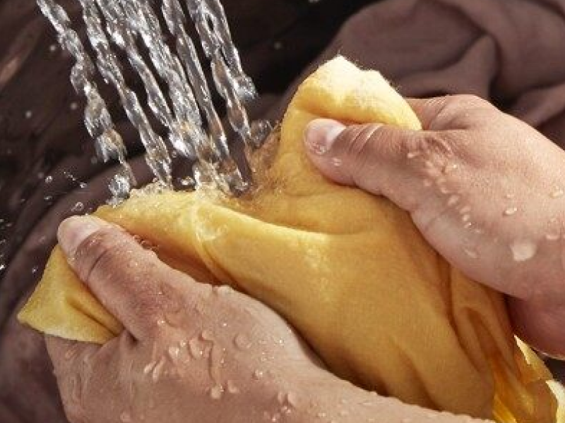 A closeup of a person adding a blanket to a Whirlpool® top load washer that’s filling with water. A closeup of a person adding a blanket to a Whirlpool® top load washer that’s filling with water.
