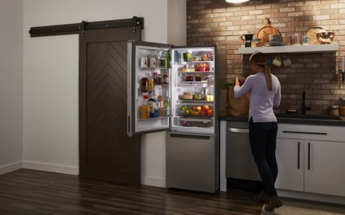 A woman next to a bottom-freezer fridge