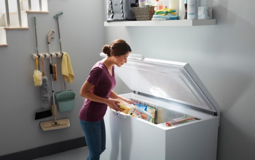 Person loading frozen food into a white chest freezer
