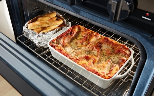 A lasagna and long rolls on a rack in the oven