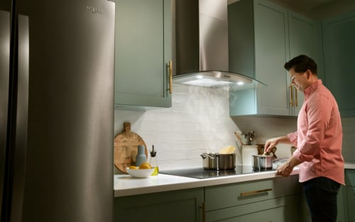 Person cooking on a cooktop with a wall mount range hood above