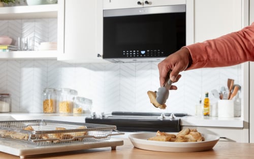 Person using tongs to remove chicken wings from air fry basket