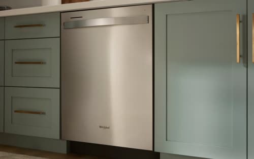 A Whirlpool® Built-In Dishwasher with Top Control and a towel handle placed between green cabinets and under white countertops