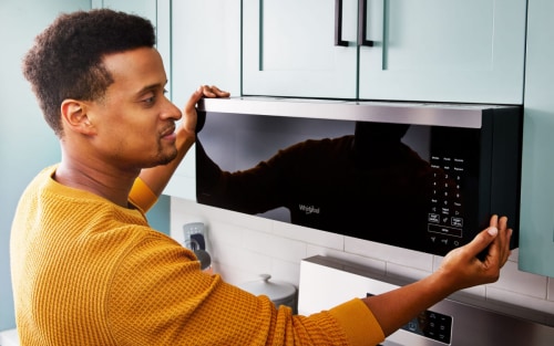 Person positioning a microwave over a stove