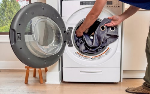 Someone putting curtains into a front load washer